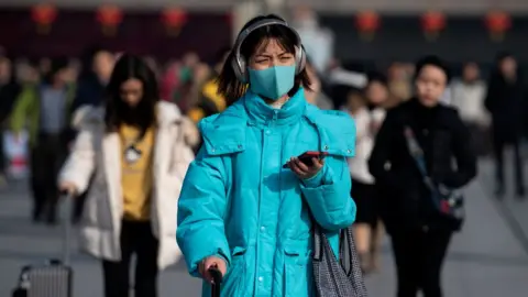 AFP A woman wears a blue face mask as she wheels luggage