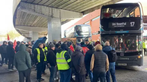 BBC Striking workers standing in front of a National Express bus