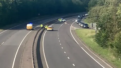View of the A1, showing police vehicles and a line of cones guiding traffic on to a slip road