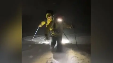 Cairngorm Mountain Rescue Team battling in the dark through deep snow with yellow jackets on and head torches.