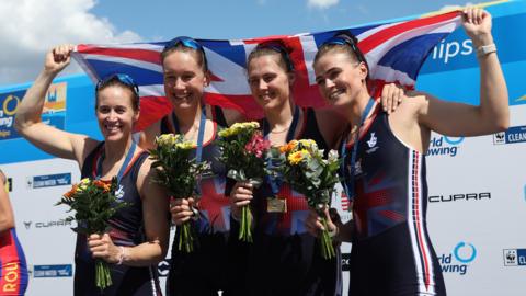 Four women are smiling each holding a bouquet of flowers. Helen and Rebecca stood at the ends of the four are holding a union jack flag  