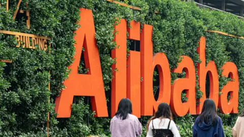 Getty Images Four women walk past an Alibaba sign.