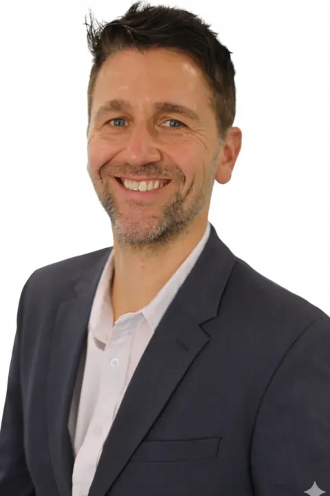 Welsh Conservatives A man in a dark suit with a white shirt smiles looking directly at the camera. He has dark hair, blue eyes and short facial hair