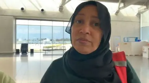 BBC Wafaa Salim pictured at Larnaca Airport in Cyprus. She has a head covering and is wearing a high visibility jacket.