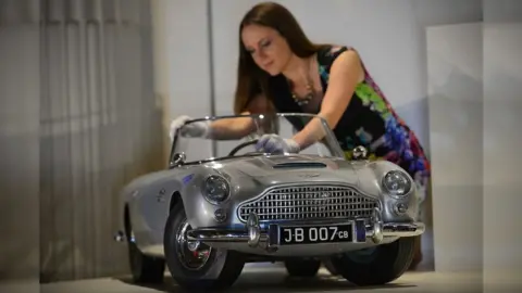 Getty Images A member of staff poses for photographers with a miniature James Bond DB5 presented to Britain's Prince Andrew by the Aston Martin company in 1965, at Buckingham Palace in central London on July 24, 2014