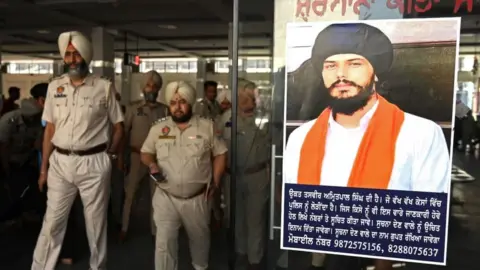 Getty Images Police stick Amritpal Singh's poster at a railway station in Amritsar on April 13, 2023.