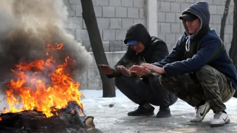 EPA Kyrgyz people warming themselves round a fire in Bishkek, Kyrgyzstan