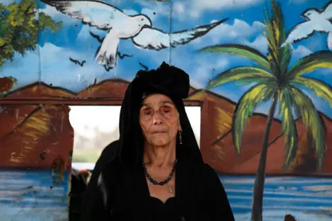 Getty Images A woman dressed in black stands in front of a painted wooden partition.