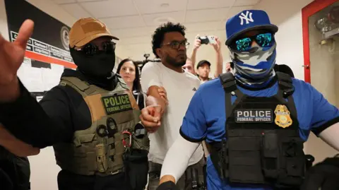 Getty Images Federal immigration officers wearing masks and sunglasses detain a man who appeared for his hearing at 26 Federal Plaza in New York City on 30 July