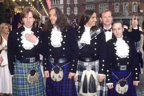 Getty Images Marti Pellow - in his long hair era - and the rest of Wet Wet Wet pose in full kilt regalia including ruffle shirts and sporrans outside a cinema in London's Leicester Square in the early 90s