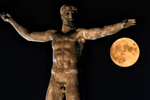 Valerie Gache / AFP The moon rises above the statue of the Ancient Greek god Poseidon in Ancient Corinth near Athens, Greece