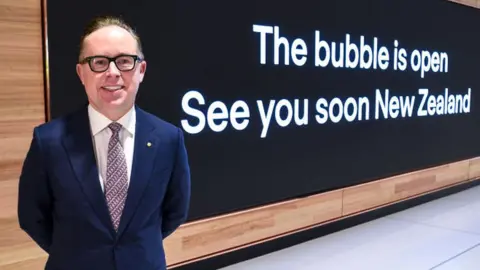 Getty Images Alan Joyce, CEO of Qantas, stands in front of a billboard as passengers board flights bound for New Zealand at Sydney's Kingsford Smith Airport on April 19, 2021.