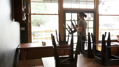 Getty Images A cafe worker puts chairs on top of tables in an empty cafe