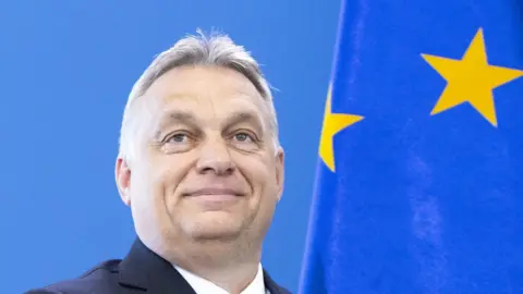 Getty Images victor Orban smiles against a blue background in which the EU flag with its bright yellow stars is visible