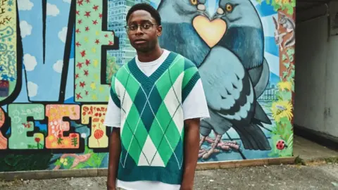 BBC/Studio Lambert Myles Kamwendo standing next to a graffiti wall in Bristol where BBC Three series Boarders was filmed