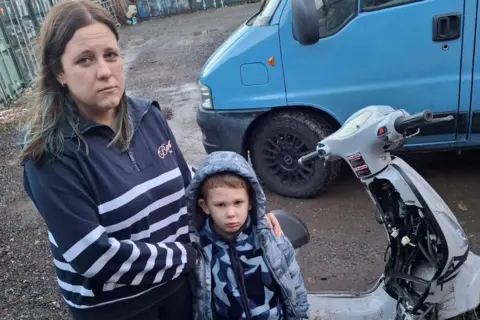 Becca Morton Becca and Joseph are standing next to the damaged motorbike. The plastic covering near the handlebars has come off and inner wires are exposed.