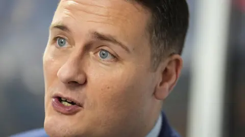 PA Media A close-up of Wes Streeting in mid-speech. He is clean shaven and wearing a blue jacket with white shirt. He has brown short hair.