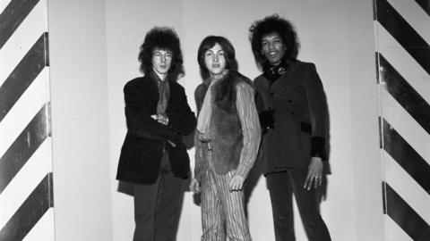 Noel Redding, John 'Mitch' Mitchell and Jimi Hendrix standing in a line together in 1967. The photo is black and white.