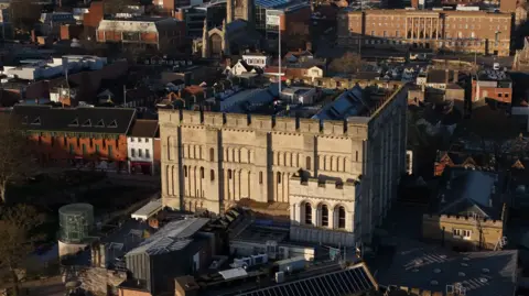A Norman castle stands on a mound in a city centre surrounded by buildings