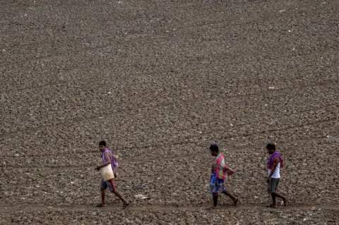 Getty Images Locals pass by the dry Puzhal reservoir on the outskirts of Chennai, India on June 29, 2019.