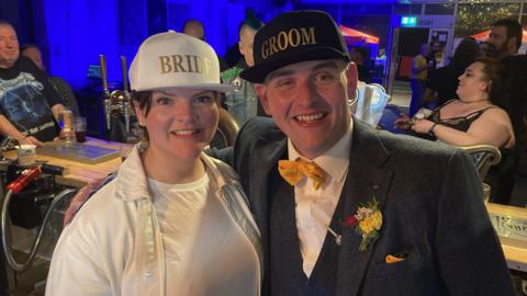 Eoin and Katie O'Mara at the venue wearing caps that say 'Bride' and 'Groom'