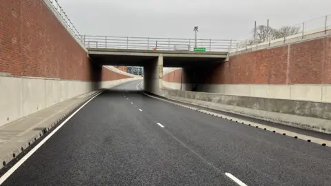 Amanda White/BBC Image of the newly built underpass. There are walls on either side. The left hand side of the road surface is visible in the shot with freshly painted white lines running along it.