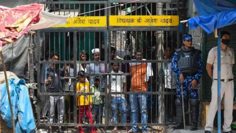 Getty Images Local residents look on as a team of Rapid Action Force (RAF) patrols the area where communal violence broke during a Shobha Yatra on Hanuman Jayanti, at Jahangirpuri, on April 17, 2022 in New Delhi, India.