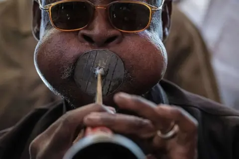 AFP A man puff his cheeks out as a he plays a horn. He is wearing glasses. A Sudanese man plays a local music instrument ahead of a meeting with Mohamed Hamdan Dagalo, also known as Himediti, deputy head of Sudan's ruling Transitional Military Council (TMC) and commander of the Rapid Support Forces (RSF) paramilitaries, in the capital Khartoum on June 18, 2019.