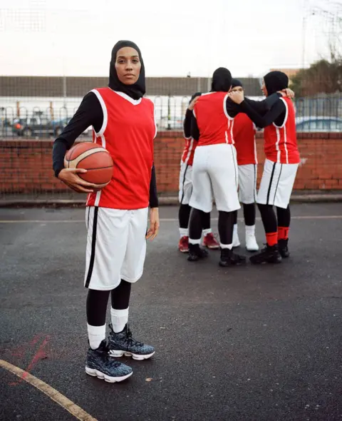 Sophie Green Portrait of Asma standing on a basketball court with her teammates behind her