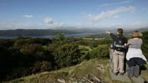 PA Media Visitors enjoying the view of Lake Windermere from the summit of Orrest Head, in the Lake District, Cumbria