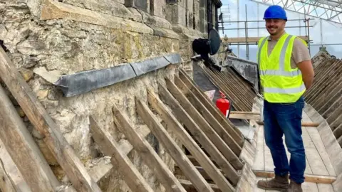 Raby Estates A man in a blue helmet and high vis jacket stands on scaffolding at the top of the building
