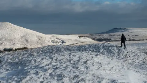 Getty Images A man walks along the Pennine Way footpath near Standedge summit past snow-covered moorland near the village of Marsden, northern England