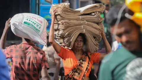 CHAMILA KARUNARATHNE/EPA-EFE/REX/Shutterstock A woman carries a stack of paper bags at a wholesale market in the commercial hub of Colombo, Sri Lanka.