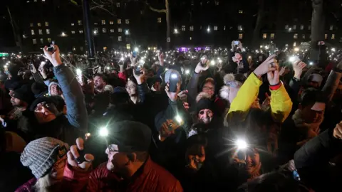 Reuters Crowds of happy people in winter clothing hold up their phone flashlights to get pictures of the display