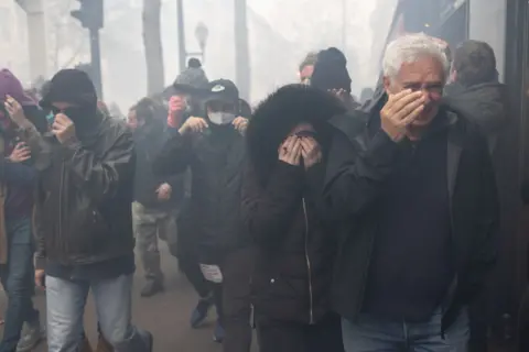 Lafargue Raphael/ABACA/REX/Shutterstock Protesters shield their eyes from tear gas during a demonstration, a week after the government pushed a pensions reform through parliament without a vote, using the article 49.3 of the constitution, in Paris on March 23, 2023.