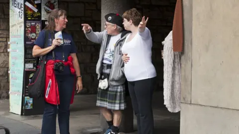 Getty Images EDINBURGH, SCOTLAND, GREAT BRITAIN - AUGUST 13: Owners of a shop targeted at tourists give directions to a visitor during the Edinburgh festival, on August 13, 2014