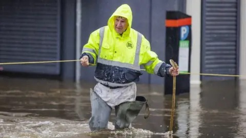 A man wearing a fluorescent coat wades through floodwater in Newry