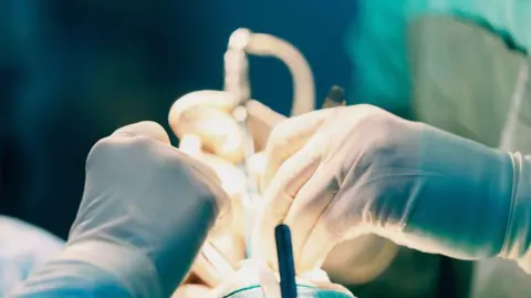 Graphixel / Getty Close up of clinicians conducting surgery. They wear latex gloves and hold surgical instruments.