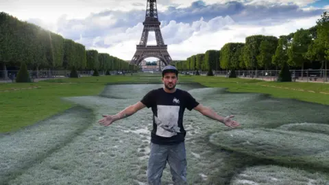 Getty Images French street artist Saype poses at the Eiffel Tower in front of his giant artwork "Beyond Walls"