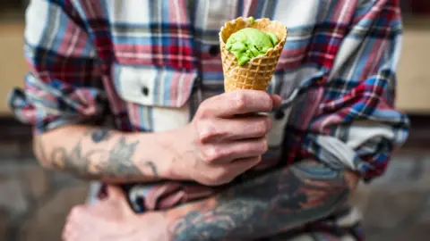 Svetlana Ivanova Slava sitting outside his cafe, Fika, holding a green matcha flavoured ice cream in a cone