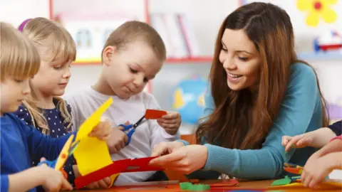 A woman helping children cut paper