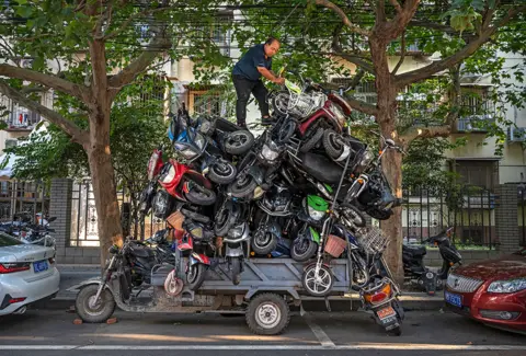 Kevin Frayer / Getty Images A man piles salvaged e-bikes and scooters on the back of a three-wheeler vehicle in Beijing, China, on 31 August 2021