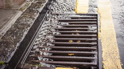 Getty Images A stream of rainwater flowing down the tarmac of a street, into a gutter