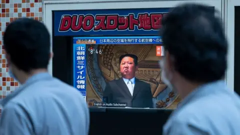 Getty Images People in Tokyo walk past a TV screen showing Kim Jong-un