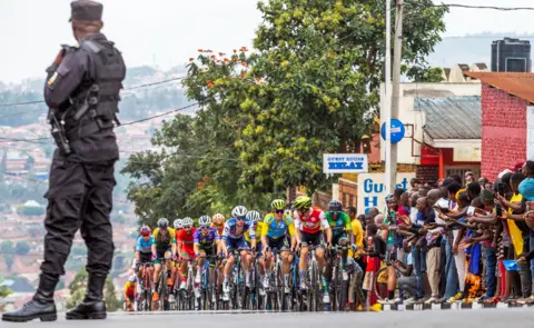 Reuters A security official looks on a cyclists taking part in the Tour de Rwanda in Kigali, Rwanda - Saturday 25 February 2023