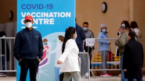 Reuters People wearing protective masks queue for booster injections of a coronavirus disease