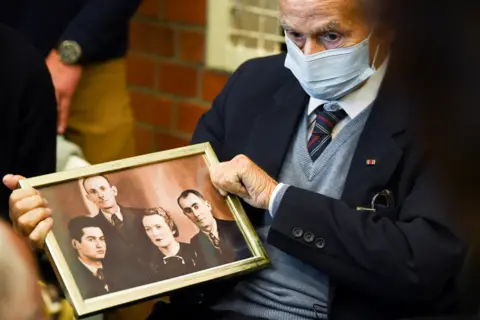 Annegret Hilse / Reuters Holocaust survivor Leon Schwarzbaum holds a picture in the courtroom during a trial against a 100-year-old former security guard of the Sachsenhausen concentration camp, at the Landgericht Neuruppin court in Brandenburg, Germany, 7 October 2021