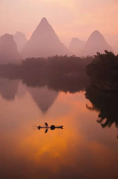 Bill Coster A sunset view of a person on a boat on water with mountains behind them