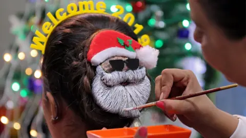 Reuters A make-up artist decorates the hair of a woman in the shape of Santa Claus during the New Year preparations in Ahmedabad, India, 31 December 2018