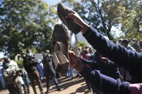 EPA A nurse shows her torn shoes as she and other health workers stage a protest at the Parirenyatwa Hospital in Harare, Zimbabwe.